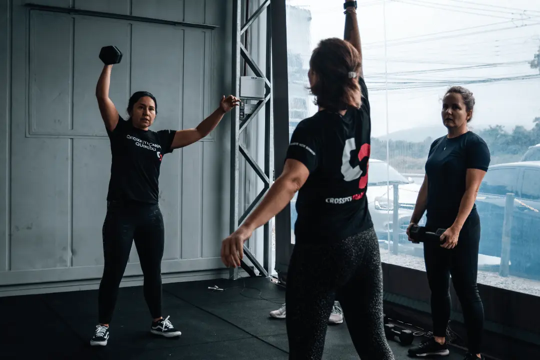 Treino funcional no CrossFit Canasvieiras, Florianópolis: elevação de halter acima da cabeça com supervisão de coaches.