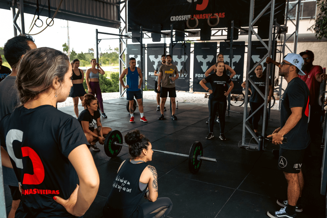 Coach do CrossFit Canasvieiras orienta a turma durante briefing técnico com barras no box em Florianópolis.